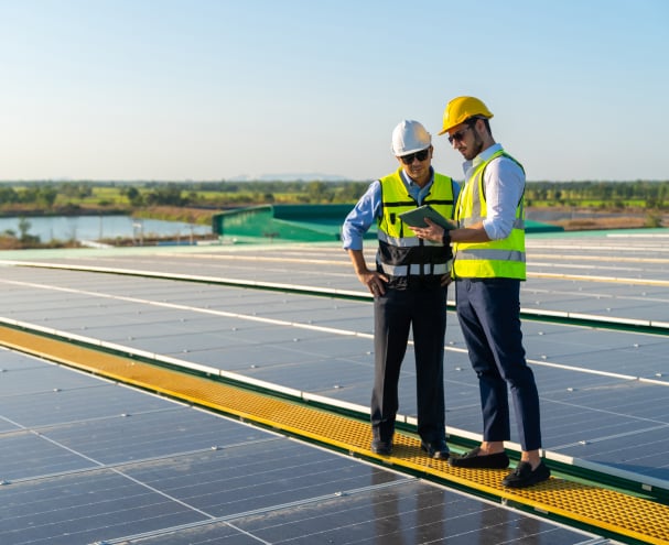 Two technicians reviewing network data on a tablet atop a solar panel installation Two technicians reviewing network data on a tablet atop a solar panel installation