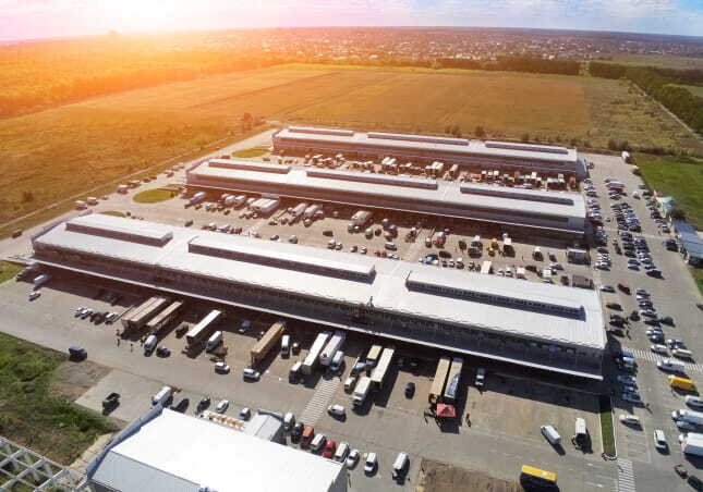Aerial view of multiple warehouse buildings with trucks parked at loading bays at sunset
